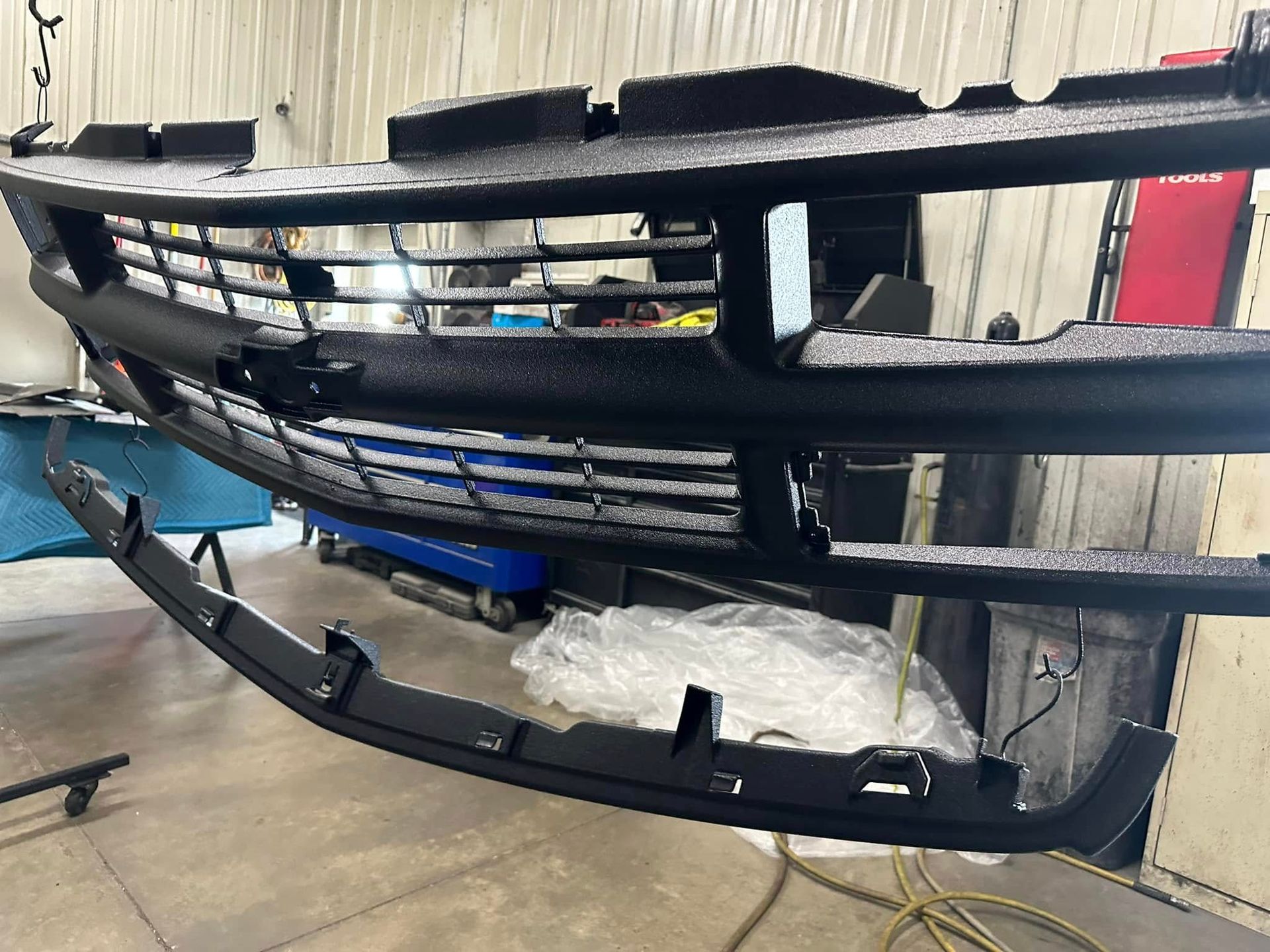 Detached black car grille and bumper parts stacked in a garage workshop.