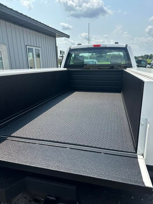 Pickup truck bed with a black textured liner and a rear ramp gate, parked beside a building.