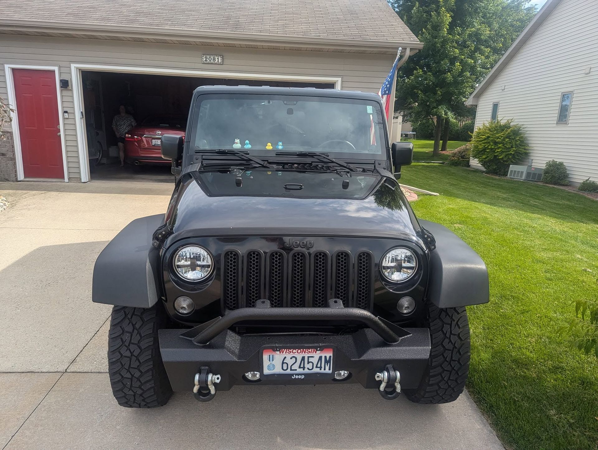 Black Jeep Wrangler parked in a driveway in front of an open garage with a red car inside