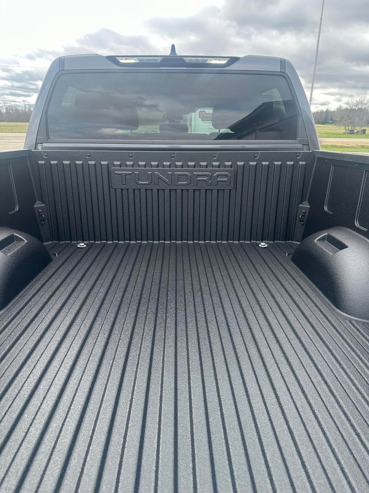 Open pickup truck bed with black spray liner, viewed from the tailgate toward the cab.