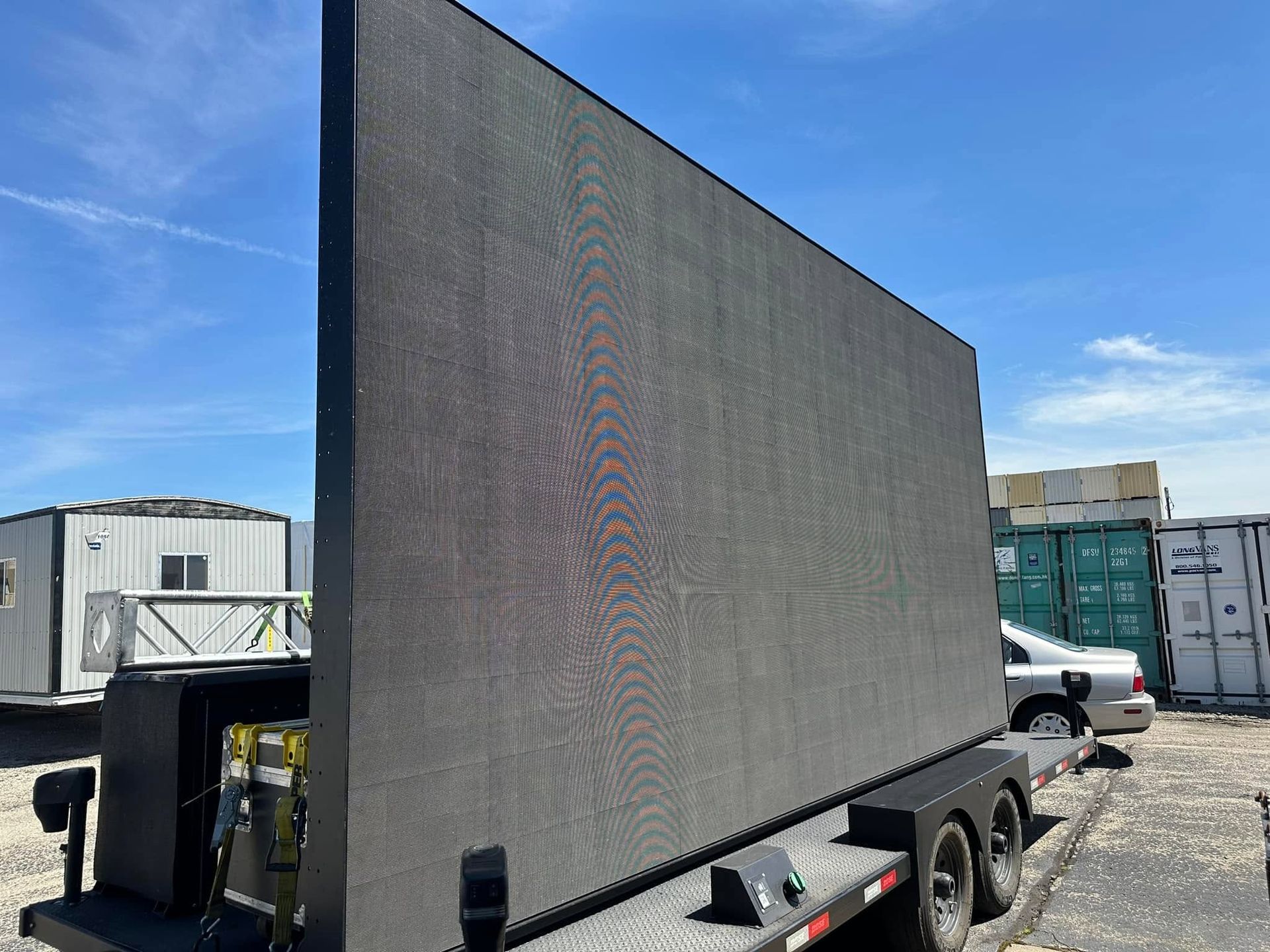 Large black trailer with a tall LED screen parked in an industrial lot under a blue sky
