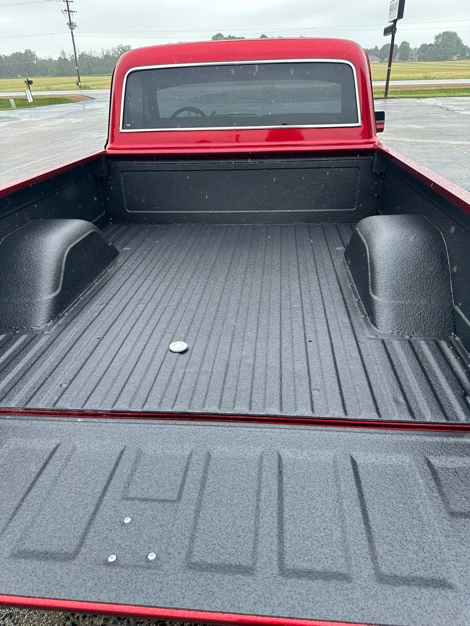 Empty red pickup truck bed on a rainy day, viewed from the tailgate.