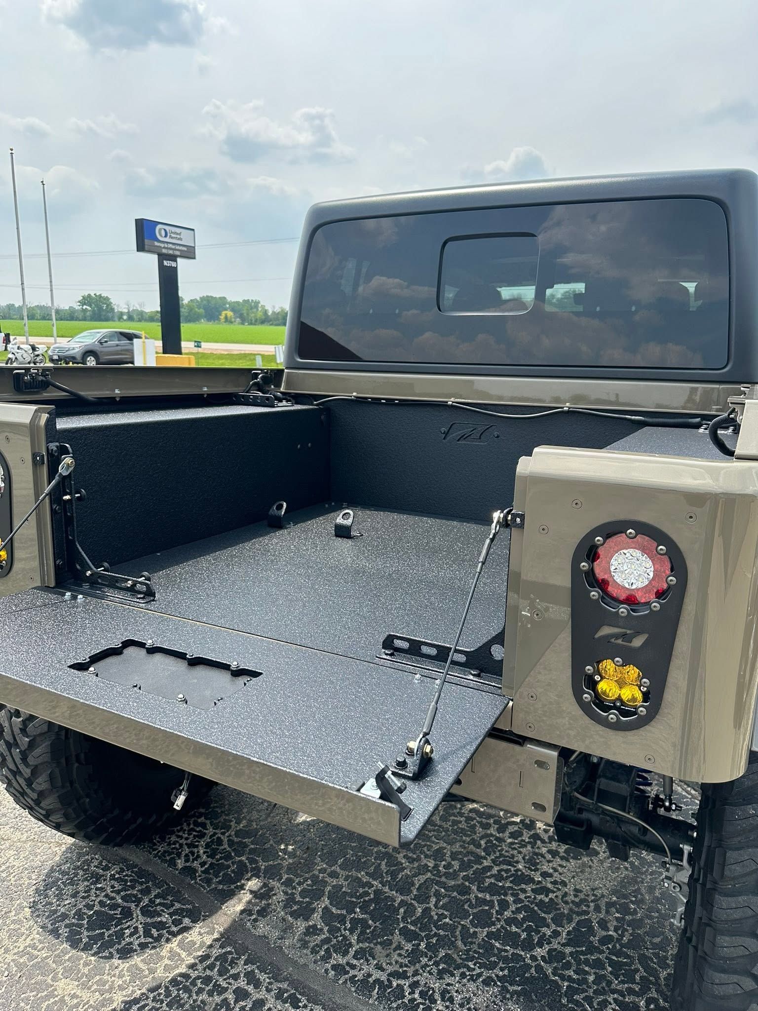Open pickup truck bed with black textured liner and rear tailgate down on a road.