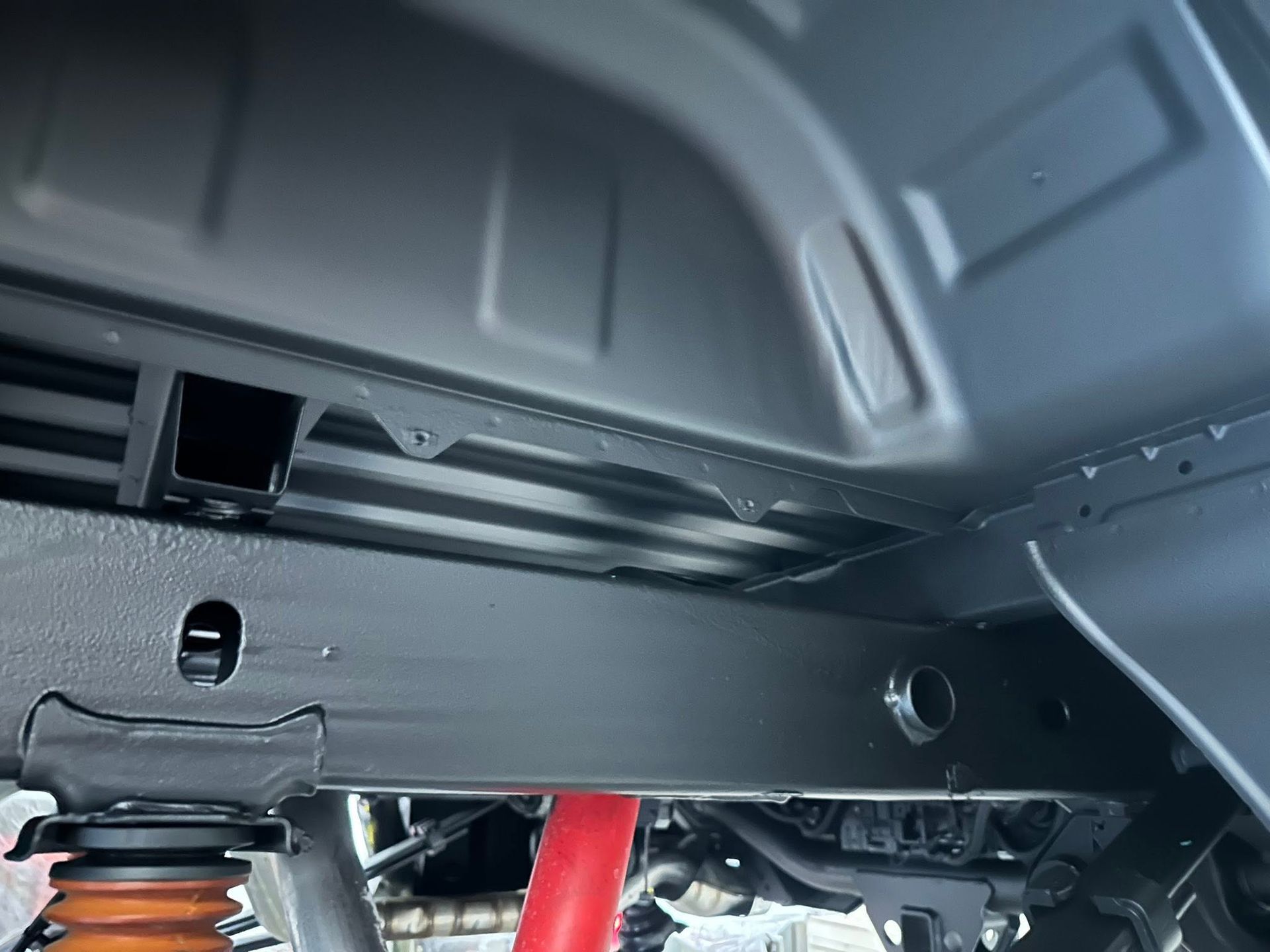 Underbody view of a vehicle with a red suspension component and black metal frame details