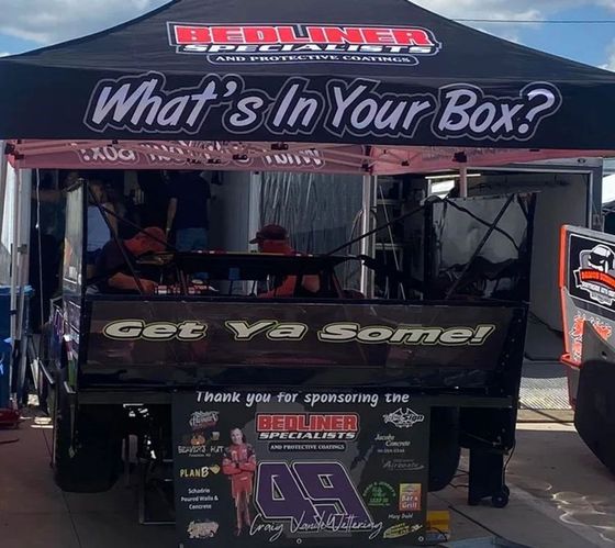 Black Redline booth tent with &ldquo;What&rsquo;s in Your Box?&rdquo; banner and &ldquo;Get ya some!&rdquo; sign at an outdoor event