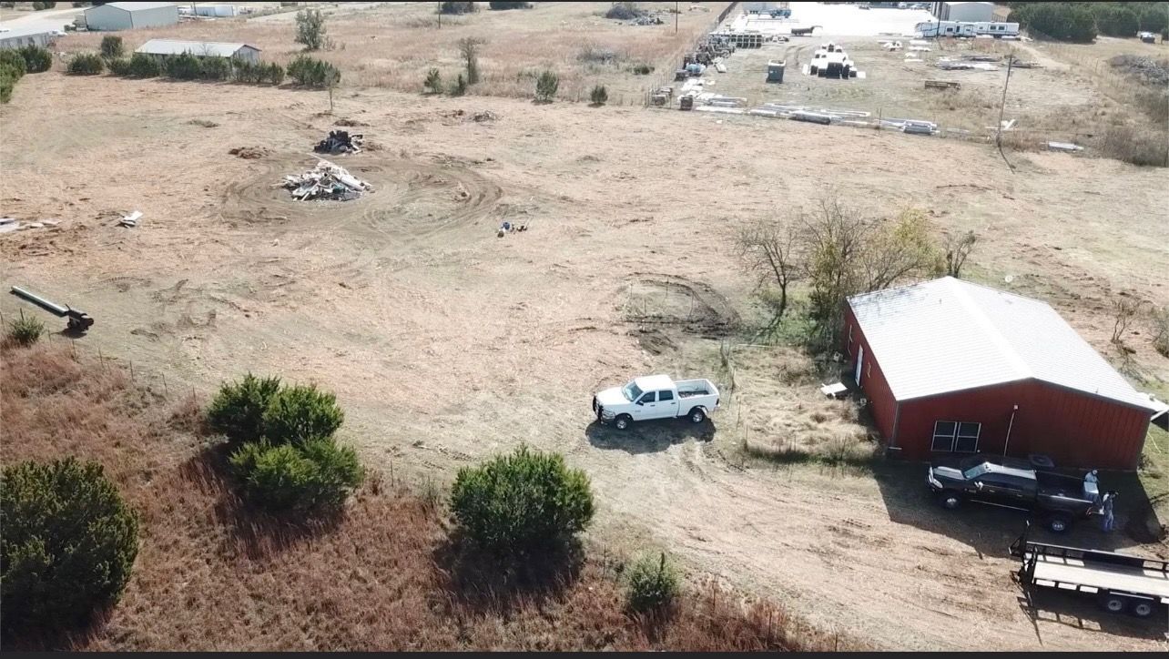 Aerial view of a brown field with a red barn, white truck, and scattered bushes.