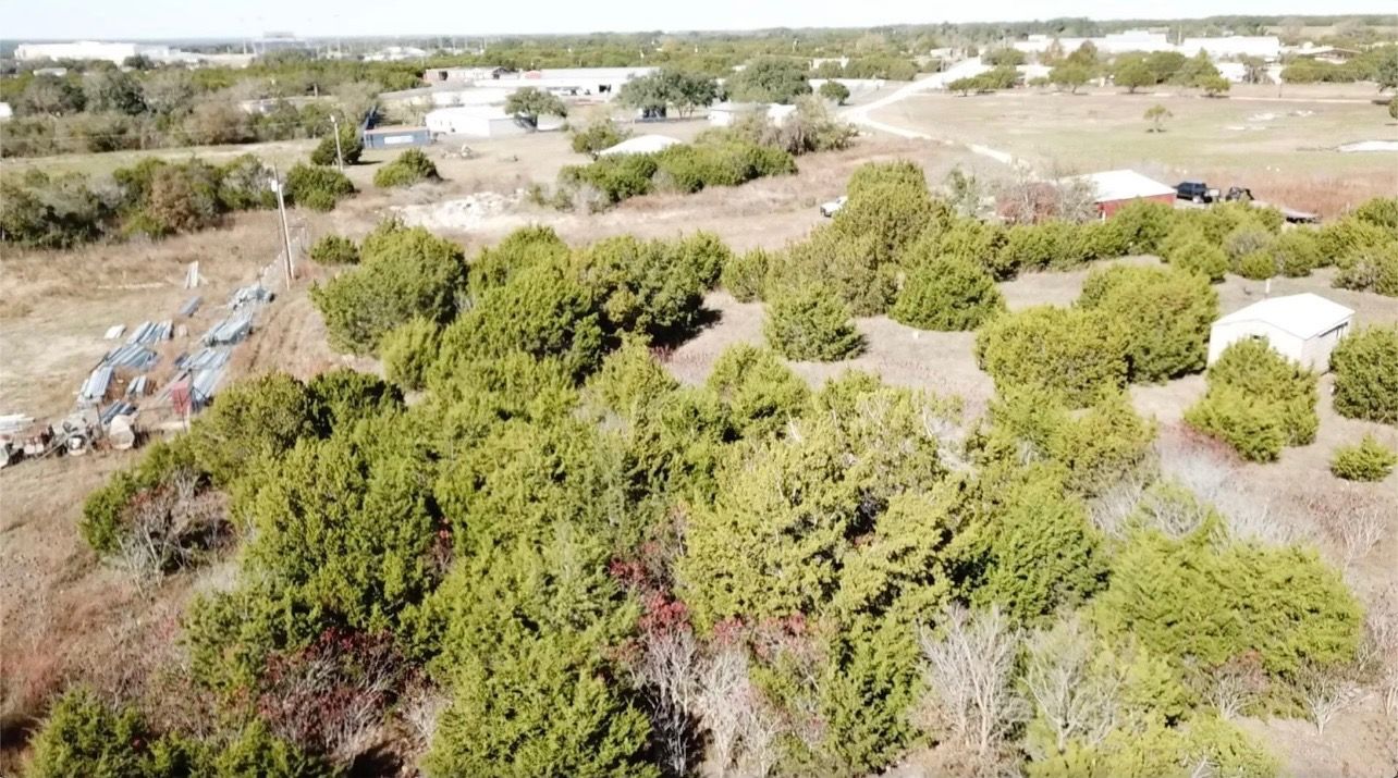 Overhead view of a landscape with green trees and brown grassy terrain under a blue sky.
