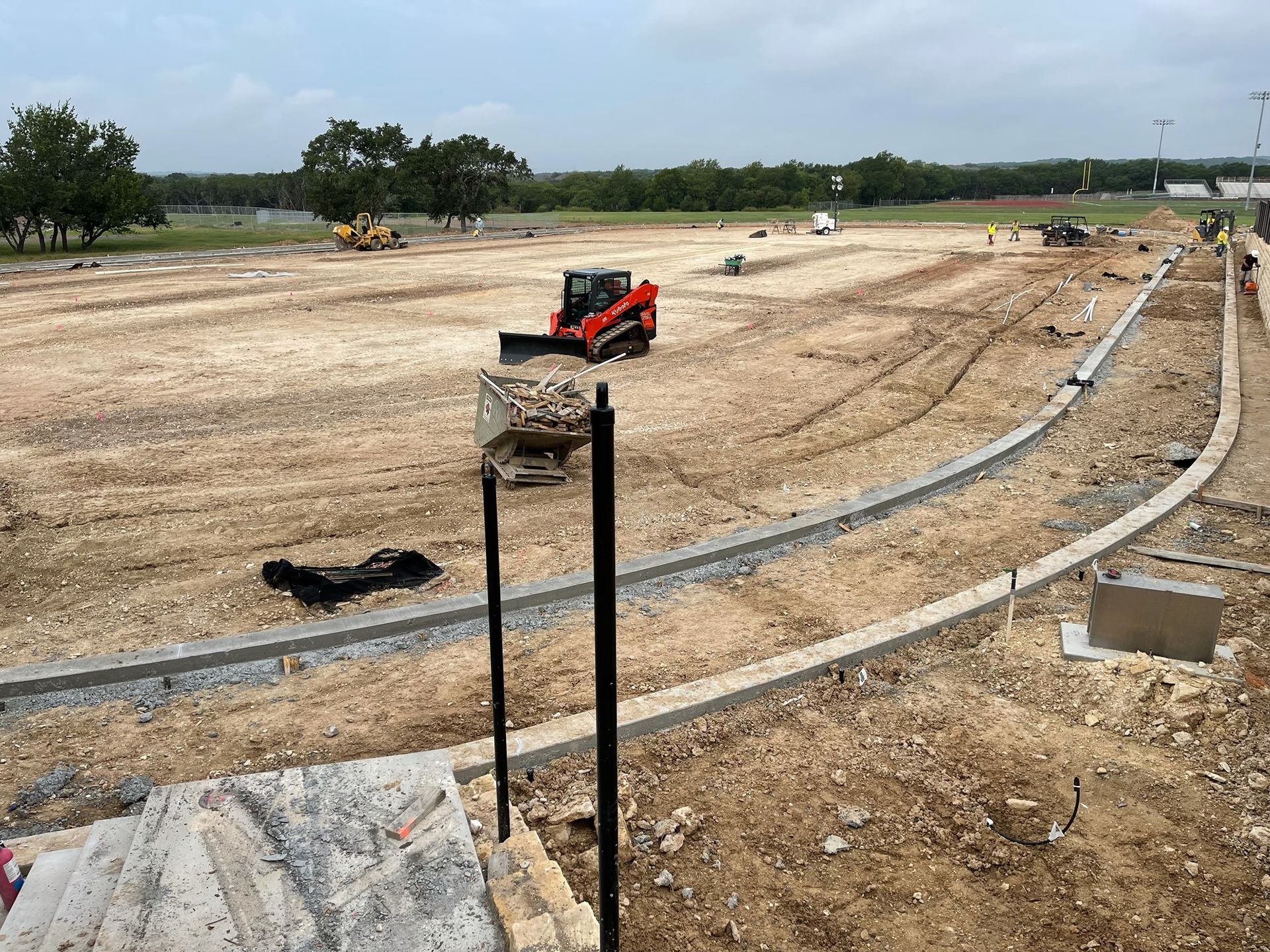 Construction site with a red skid steer, dirt, and concrete curb in progress.