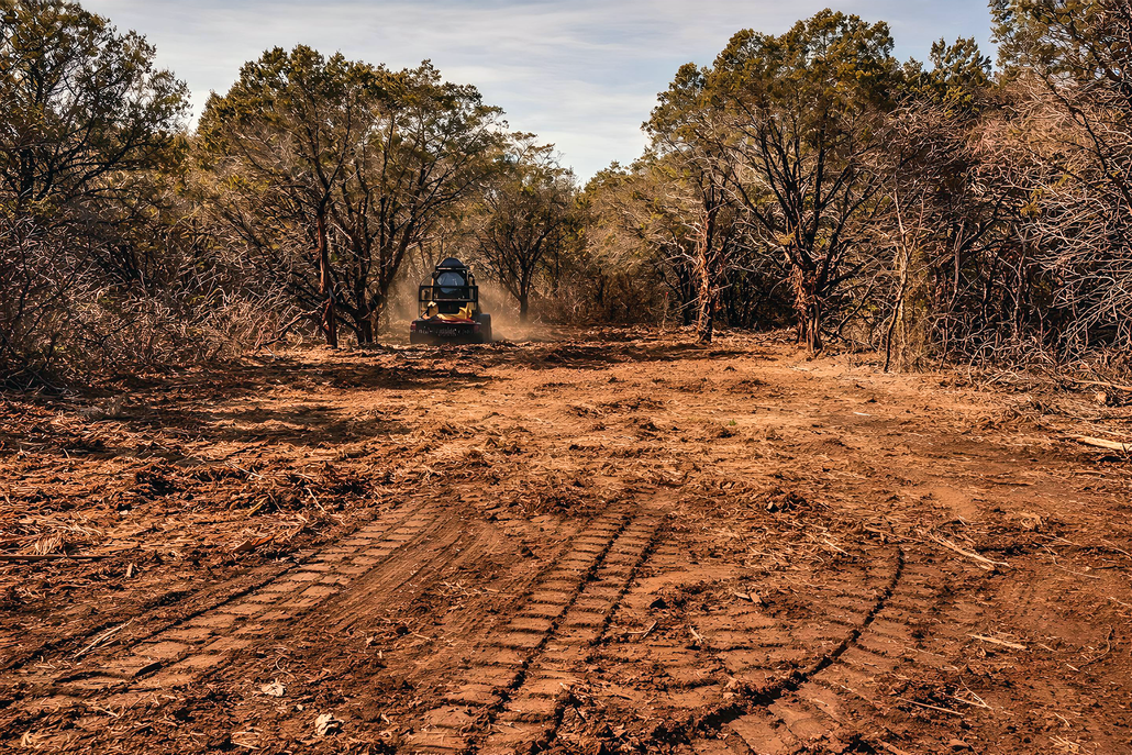 An ATV traveling through a dirt path, surrounded by trees and shrubbery, kicking up dust.