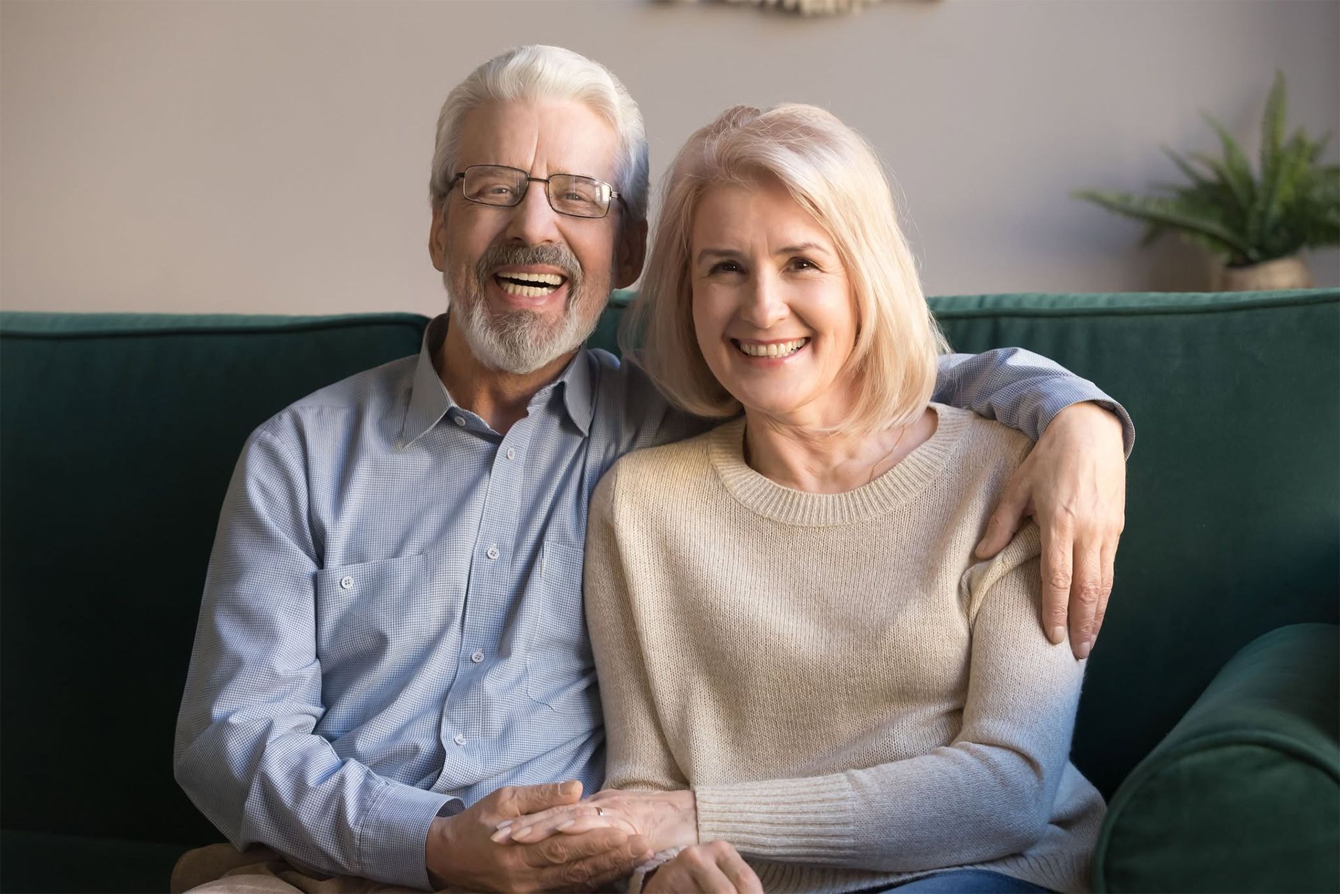 An elderly couple is sitting on a couch and smiling for the camera
