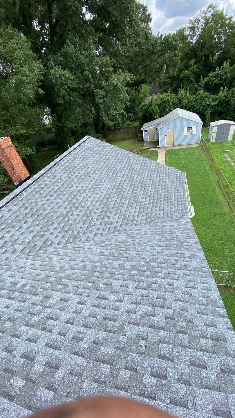 Gray asphalt shingle roof on a house, with a grassy area and trees in the background.