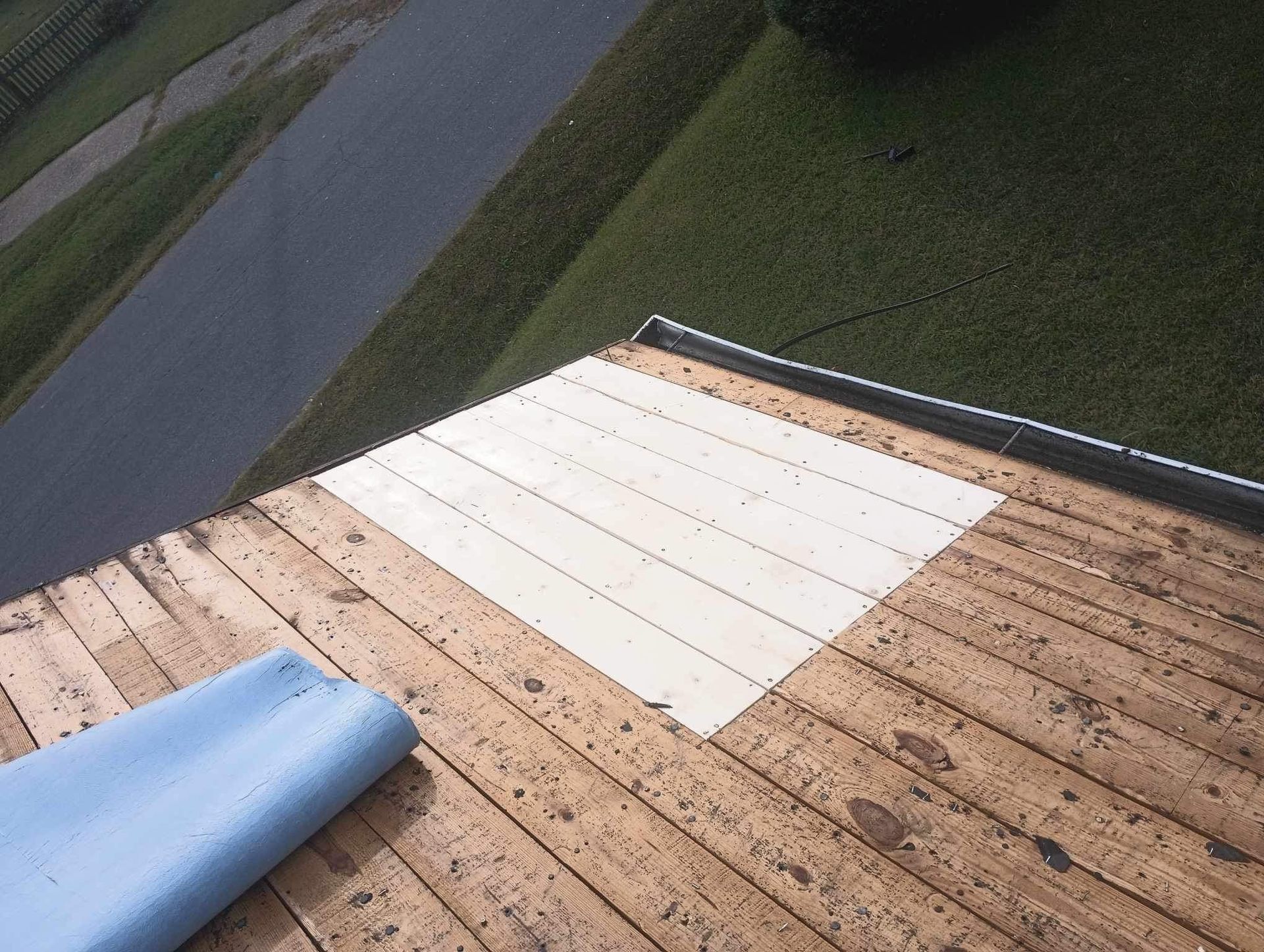 View of a roof with a patched white section, next to a blue sheet, near a driveway and grass.