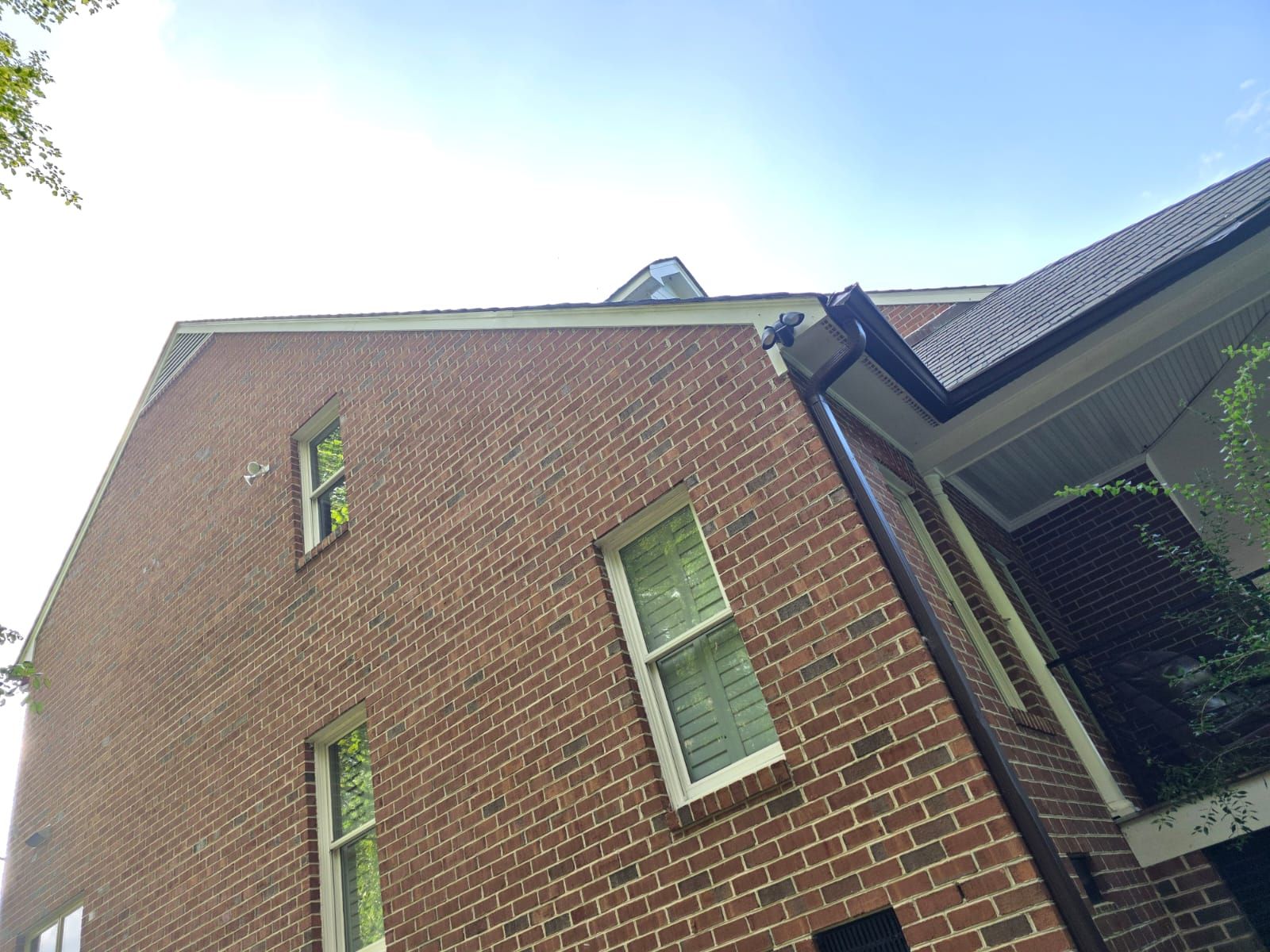 Brick house exterior with three windows, dark gutters, and blue sky.