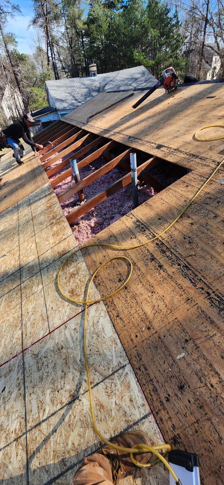 Roof under construction; opening exposing insulation.  Worker and equipment visible. Sunny day.