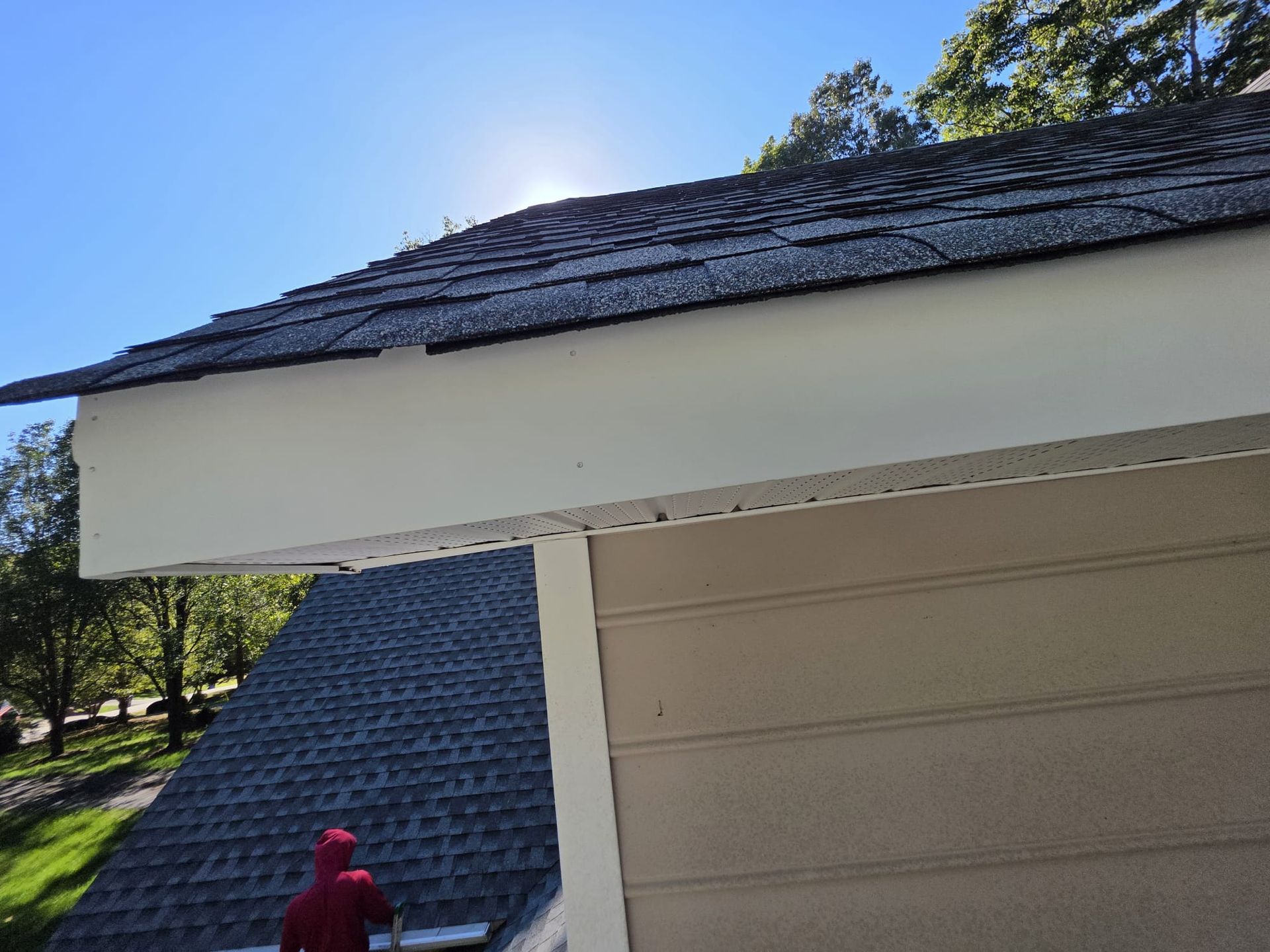 Roof with dark shingles and white trim, sunlight above. Beige siding below.