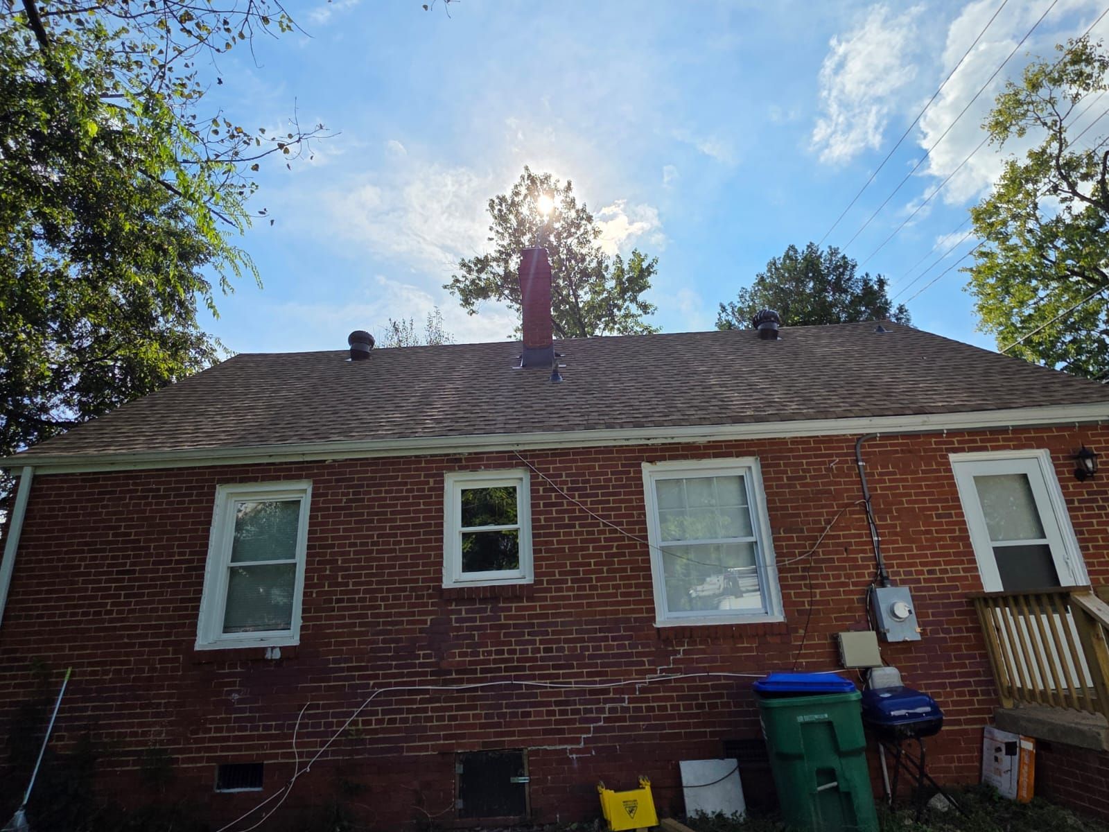 Brick house with a brown roof and a chimney against a sunny sky.