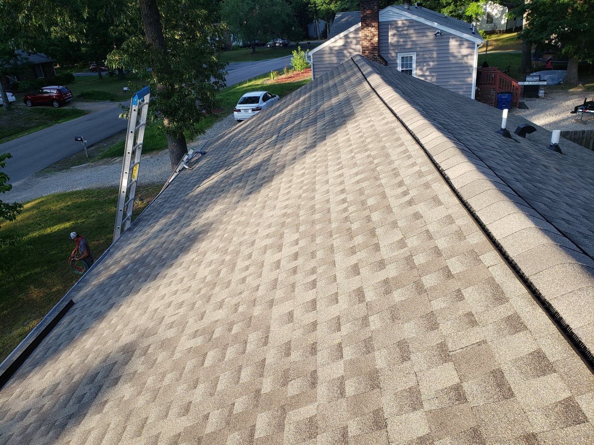 Workers on a gray shingled roof, trees, and street in the background.