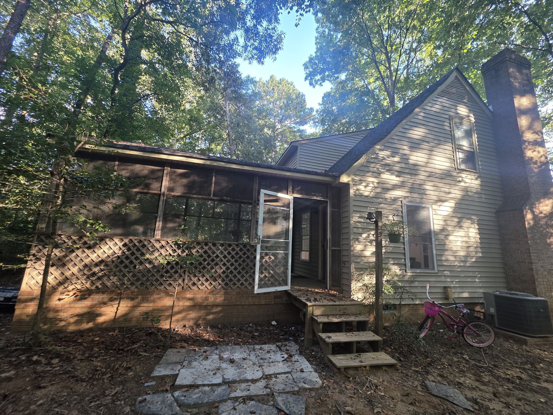 Dilapidated cabin in wooded area, with open door and a child's bicycle leaning against the wall.