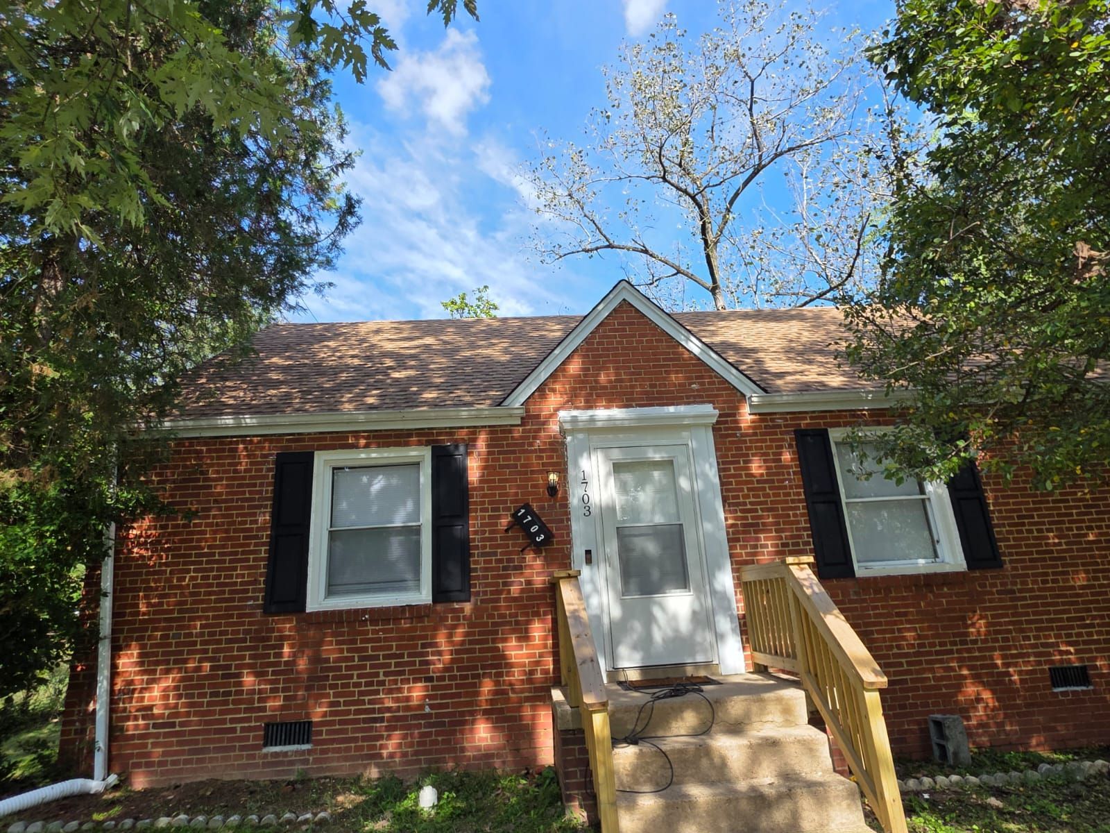 Brick house with brown roof, white door, black shutters, and steps leading to entrance. Blue sky.