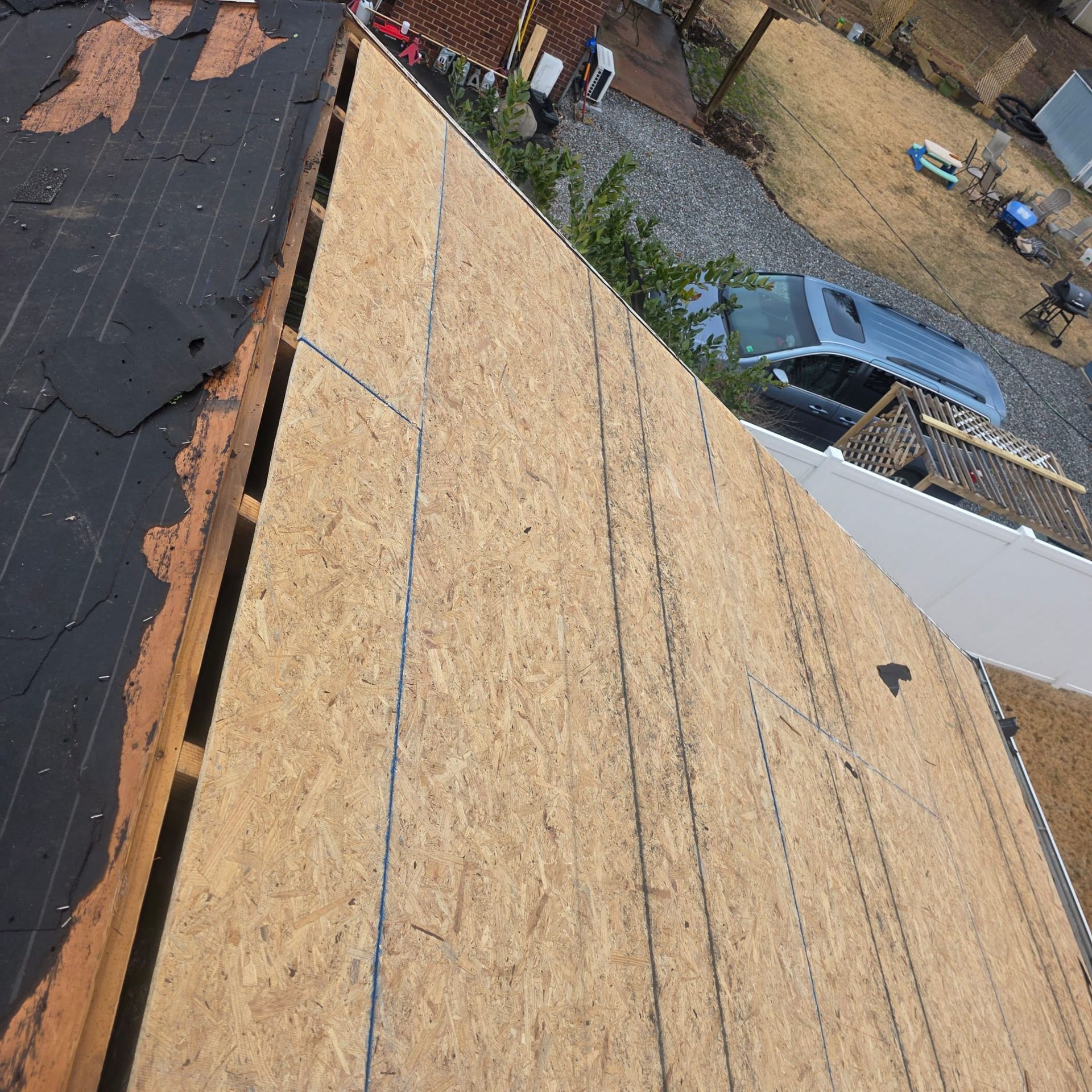 Overhead view of a roof under construction. OSB sheathing is installed on part of the roof. Old shingles remain on the other part.