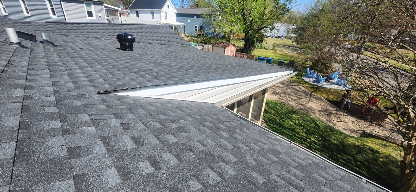 Gray shingle roof, chimney, and a glimpse of a yard with trees and blue tarps.