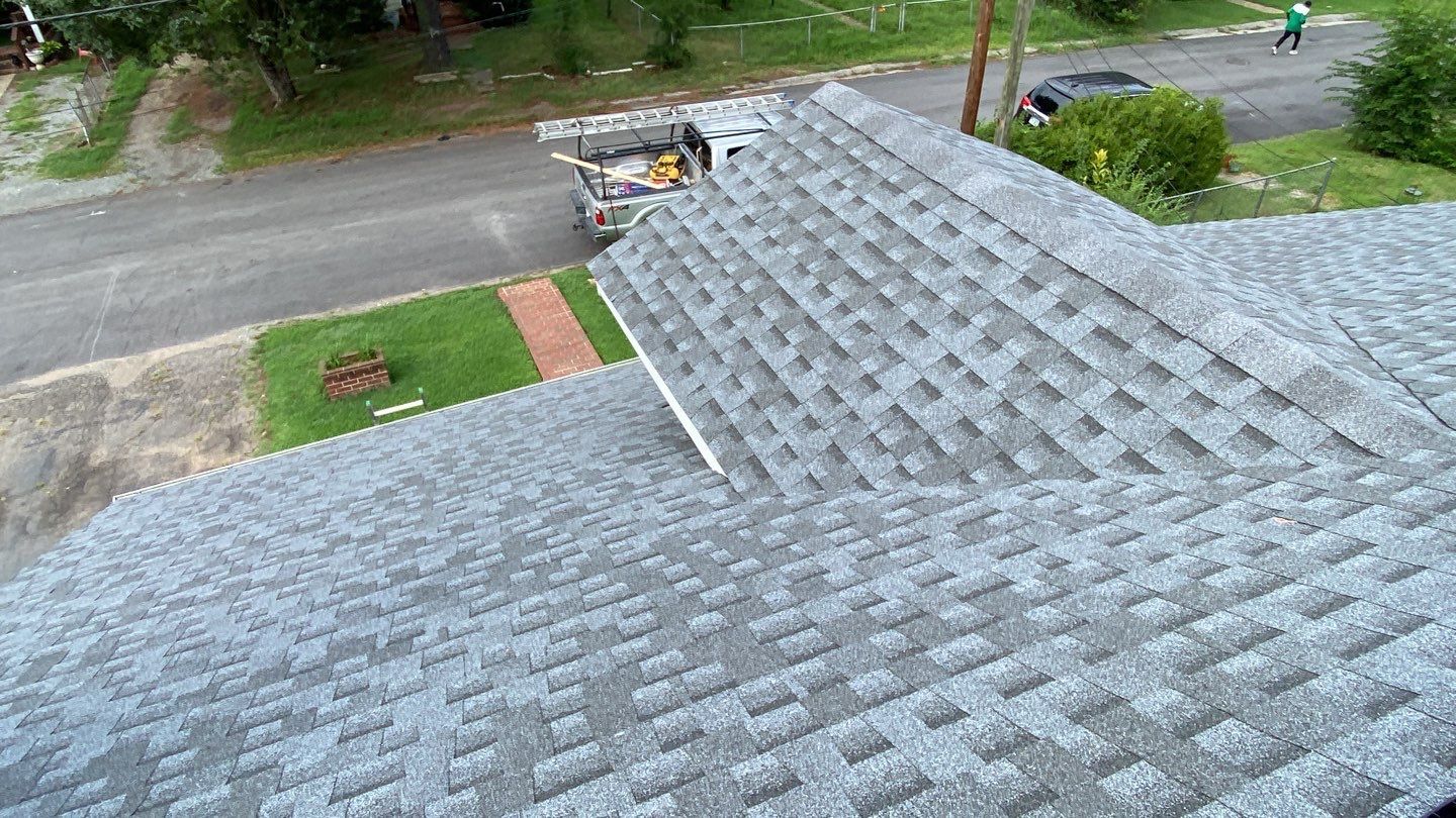 Gray asphalt shingle roof on a house, with a street and yard visible below.