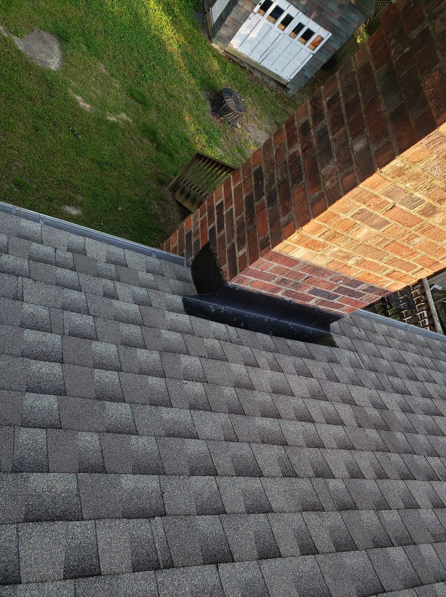 Gray shingled roof with a brick chimney. Flashing visible where roof meets chimney.