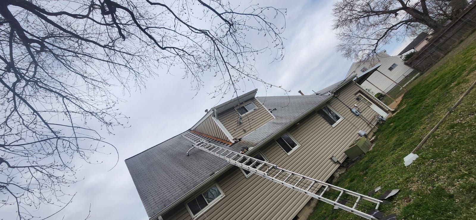 A house with a ladder propped up against the roof. Overcast day.
