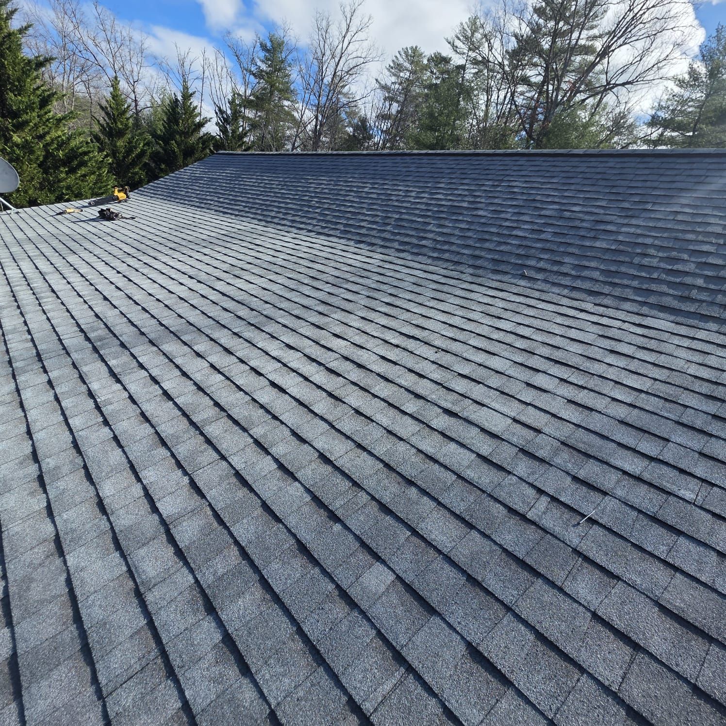 Close-up view of a dark gray asphalt shingle roof under a partly cloudy blue sky.