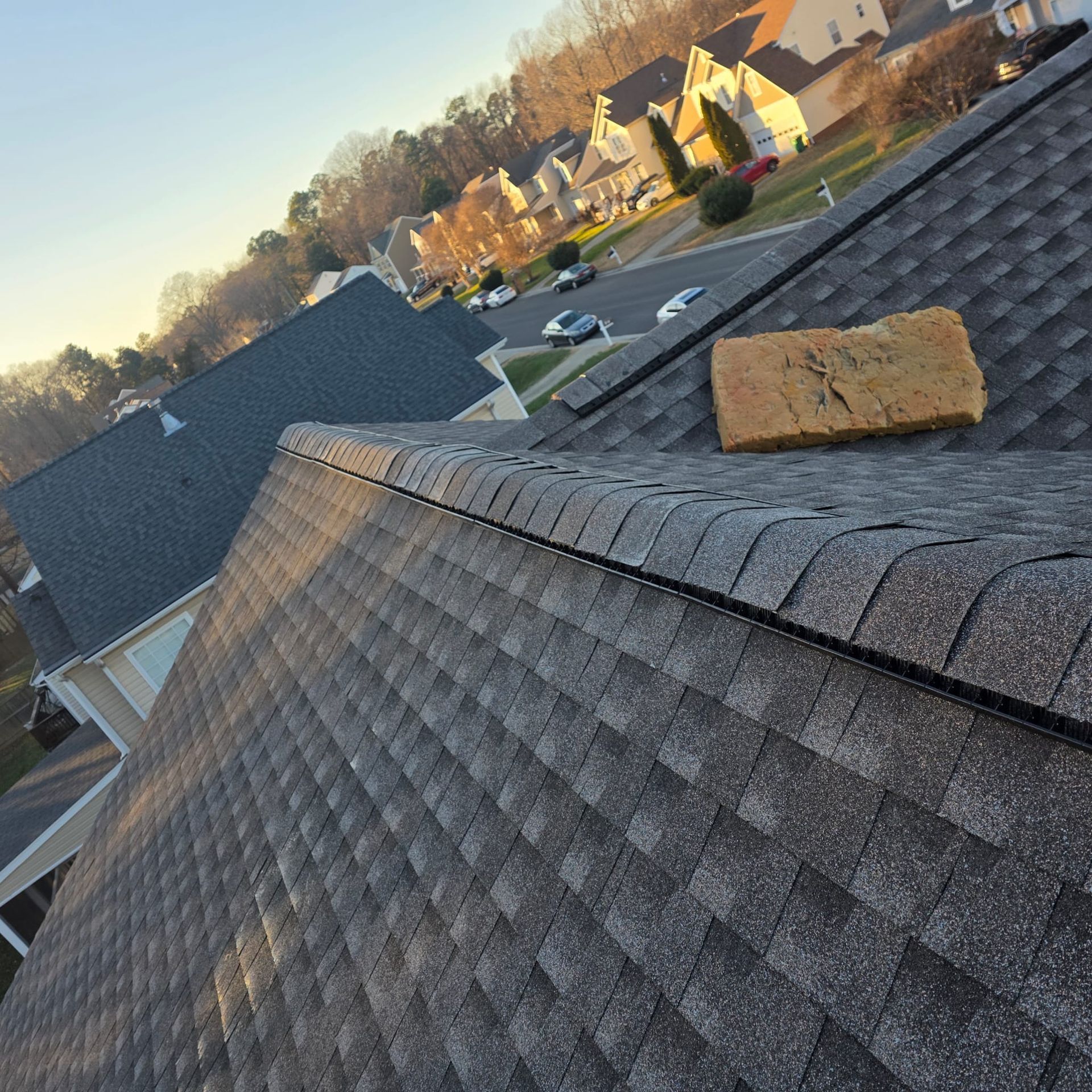 Rooftop view of gray shingles, a brick, and suburban homes in the background.