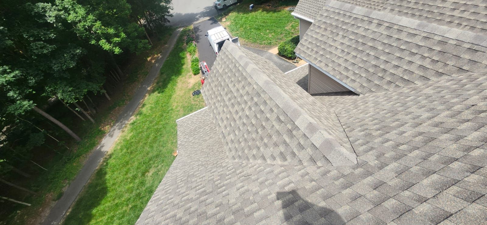 View from above of a house roof, grass, trees, and a road.