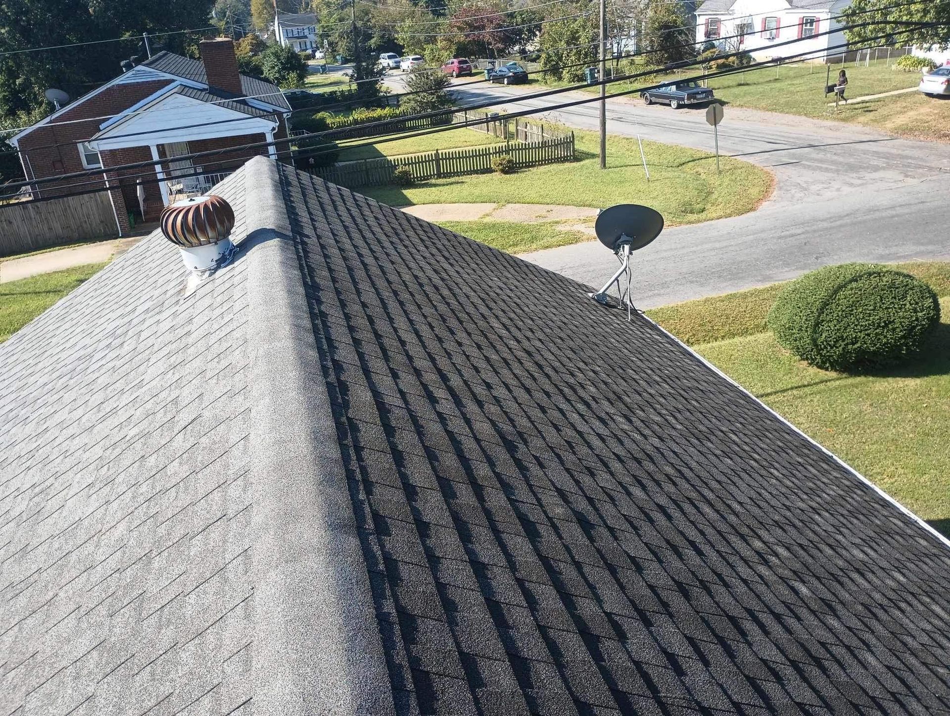 View of a shingled roof with a vent and satellite dish. Houses and street in the background.