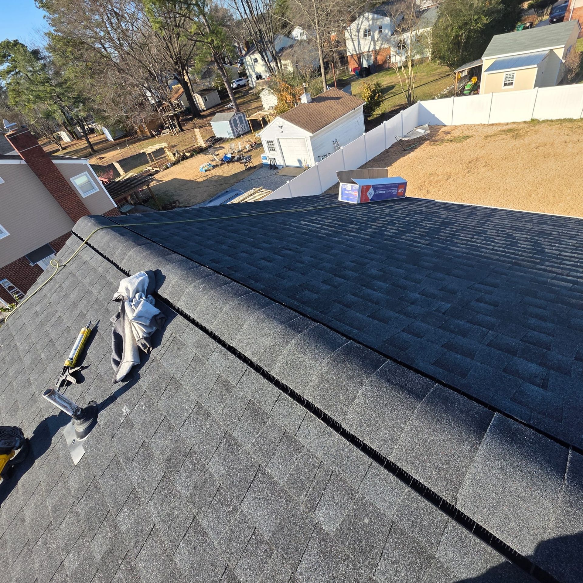 Black asphalt shingle roof, tools visible, residential neighborhood in background.