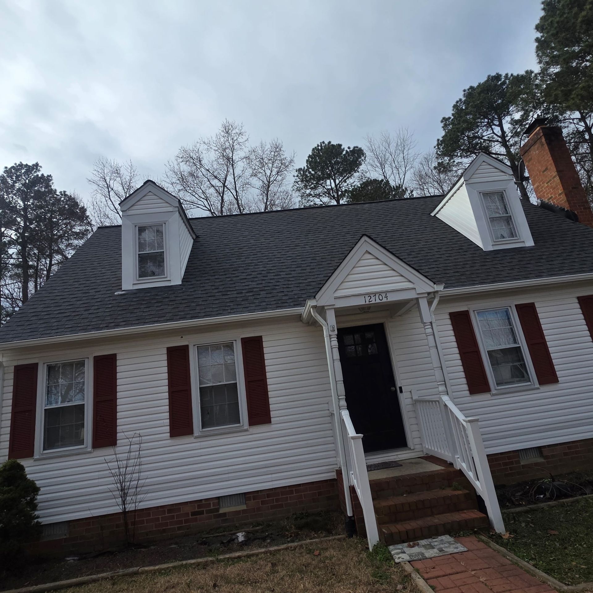 White house with red shutters, black door, and brick chimney under a cloudy sky.