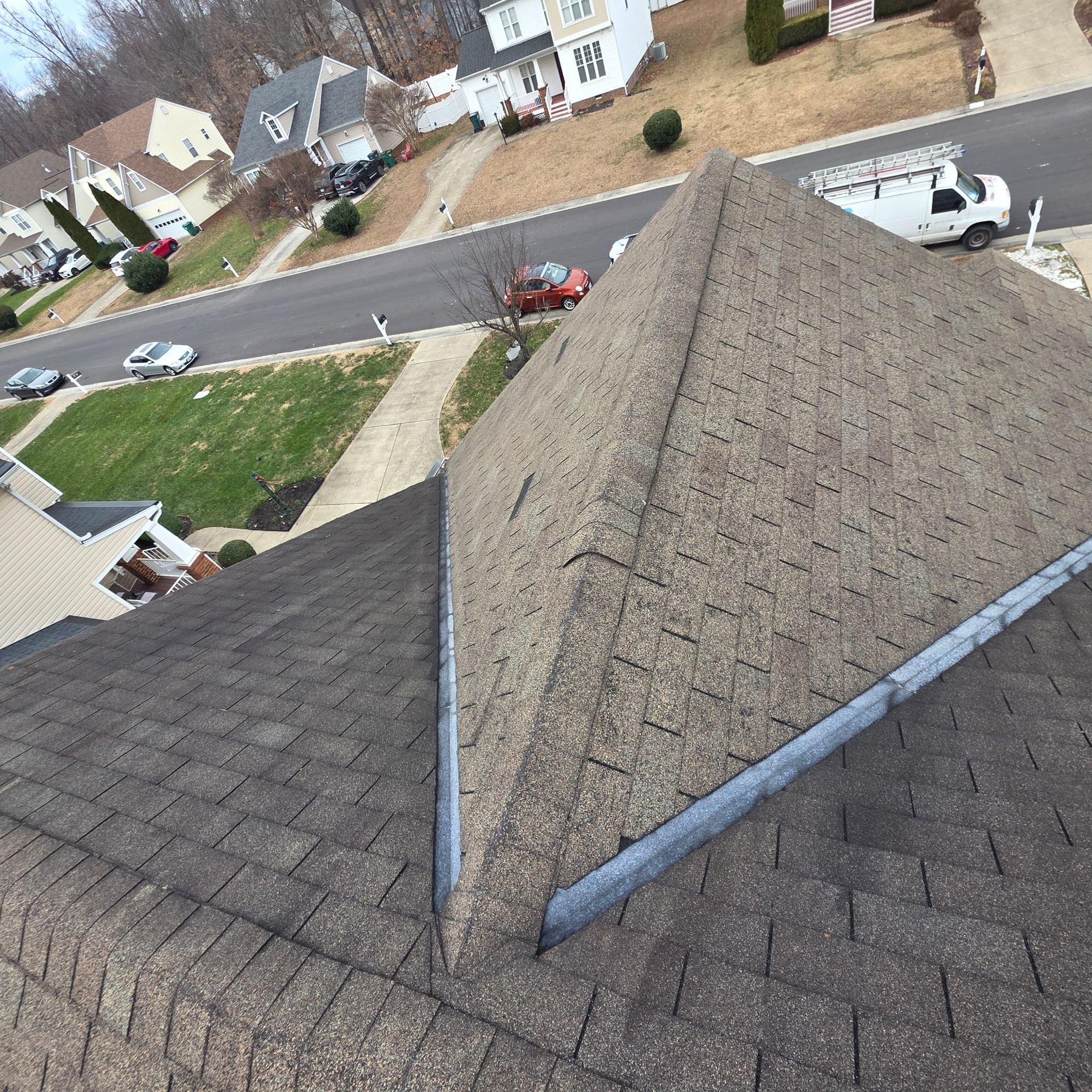 Overhead view of a house roof with a gray asphalt shingle roof in a suburban setting.