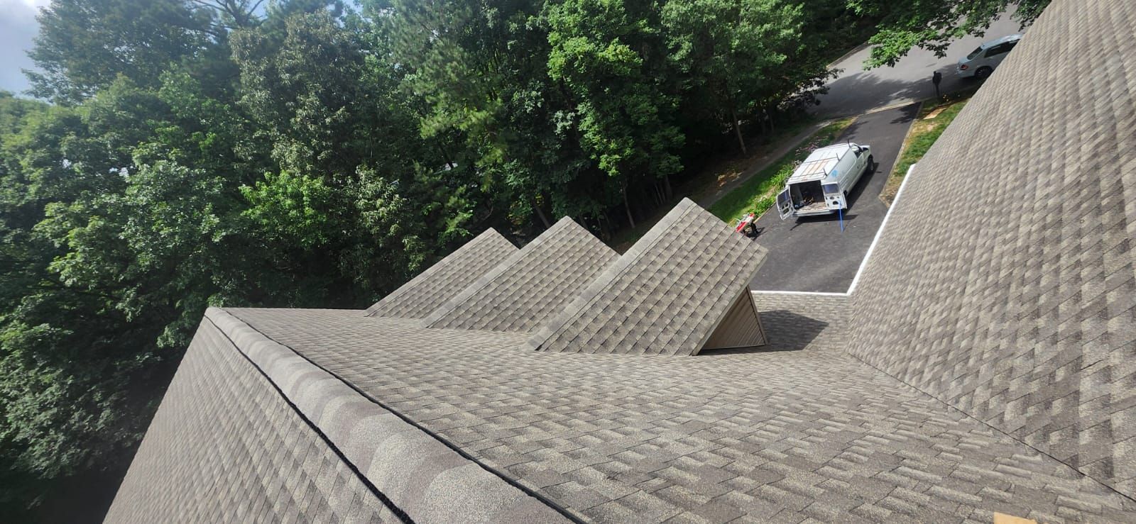 View from a rooftop, showing a vehicle on a driveway, surrounded by green trees.