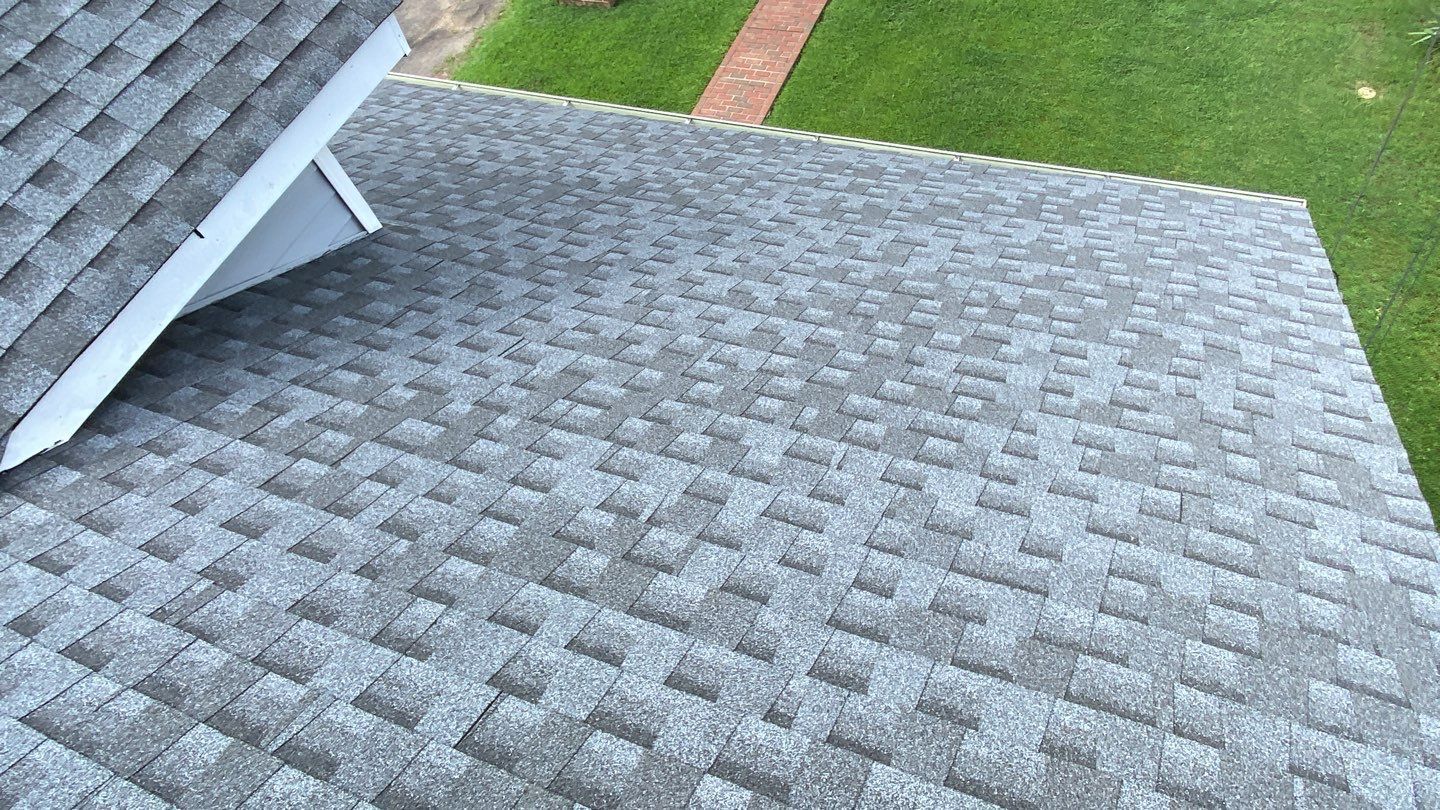 Gray asphalt shingle roof on a house, angled view, green grass in background.