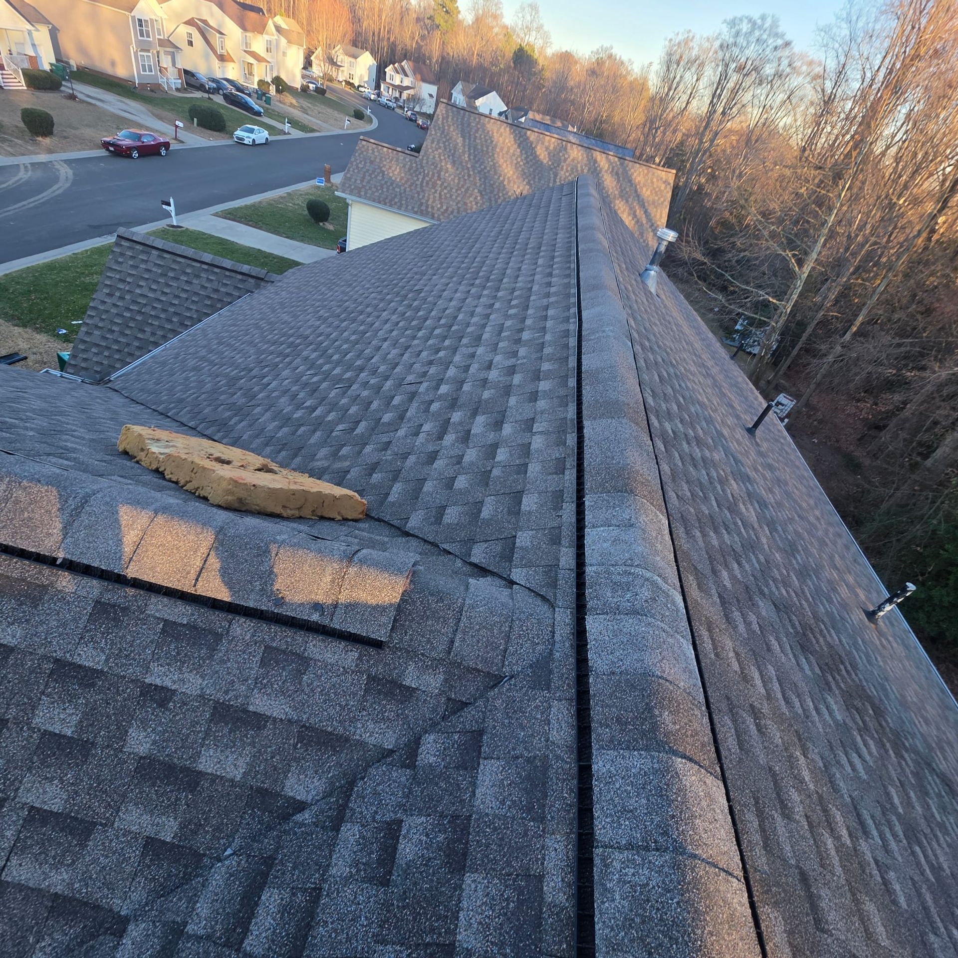 View of a residential roof with shingles, a brick, and a neighborhood in the background.