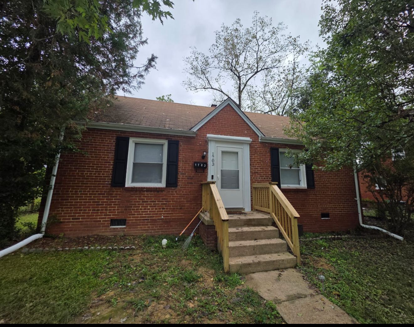 Red brick bungalow with a white door, black shutters, and wooden steps.