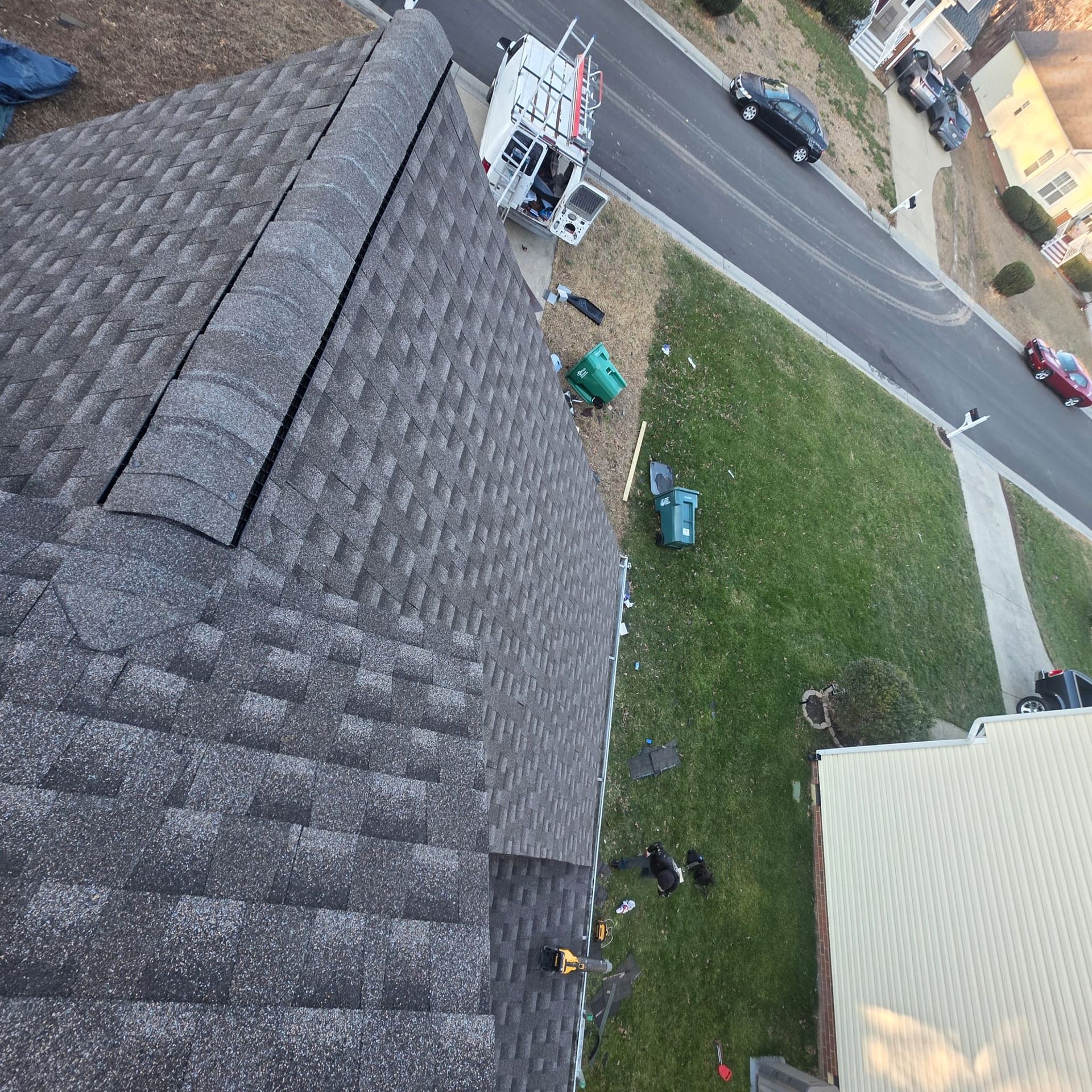 Rooftop with installed asphalt shingles, looking down at a lawn, street, and parked vehicles.