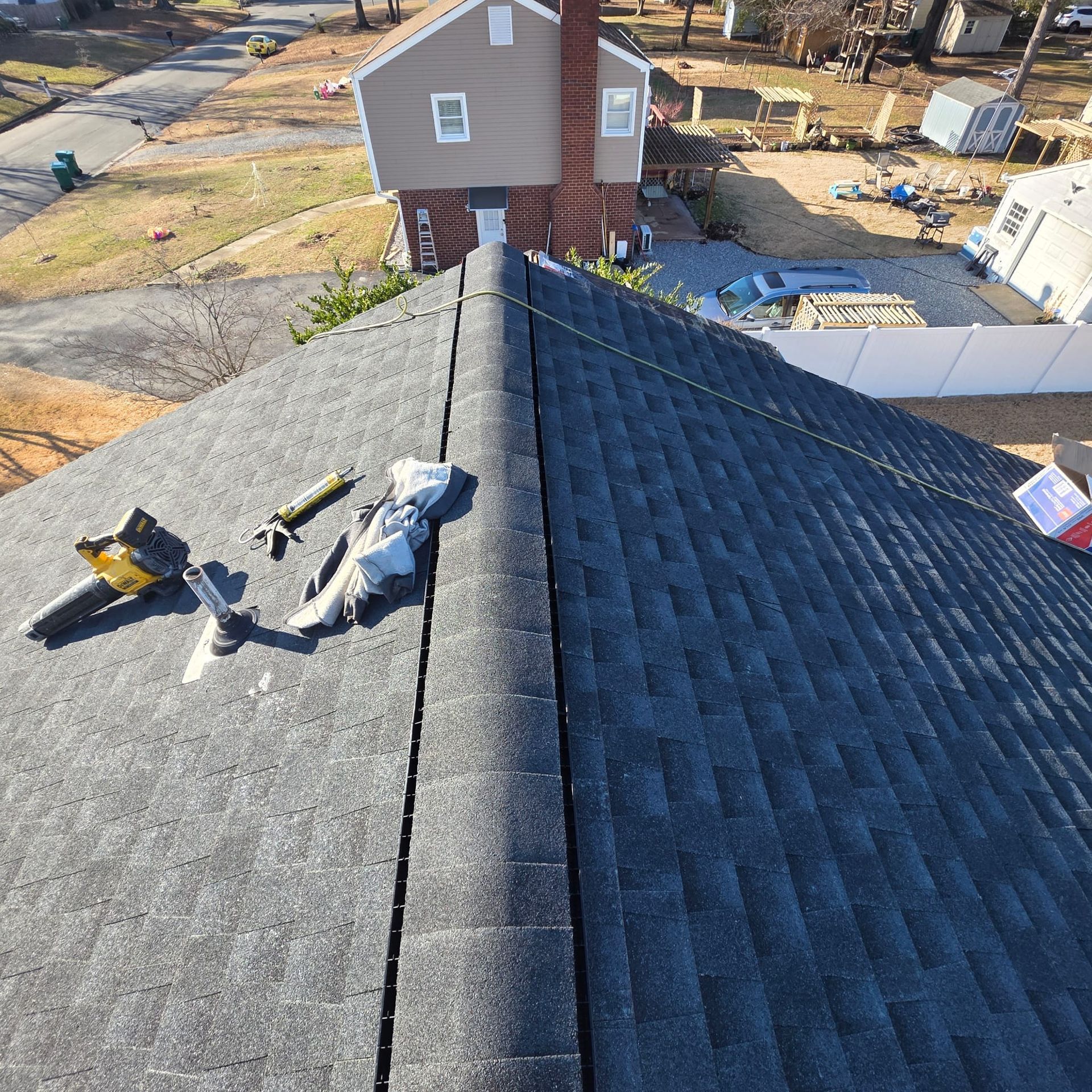Roof with gray shingles, tools, and a brick chimney in the background. Sunny day.
