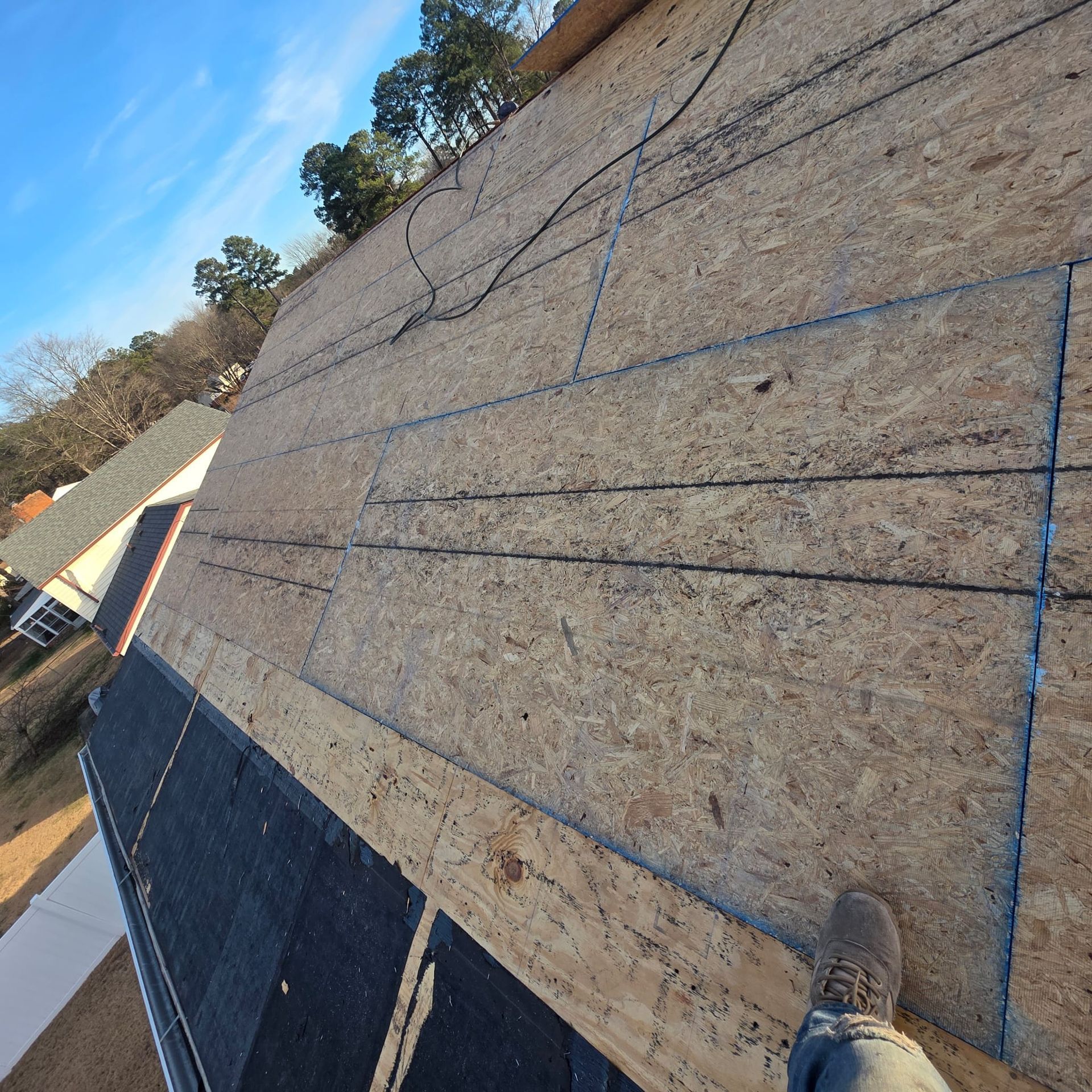 Roof under construction, showing plywood sheathing, partially installed shingles, and a work boot.