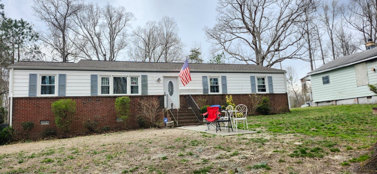 A white ranch-style house with blue shutters, a brick facade, and an American flag.