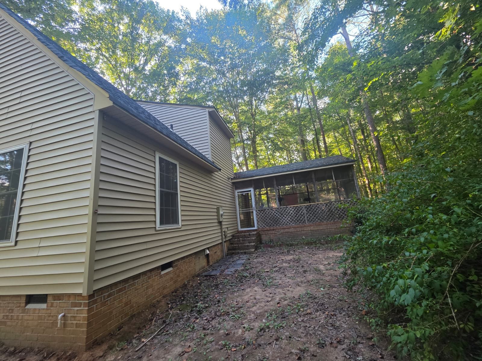 Side view of a house with light green siding and a covered porch in a wooded area.