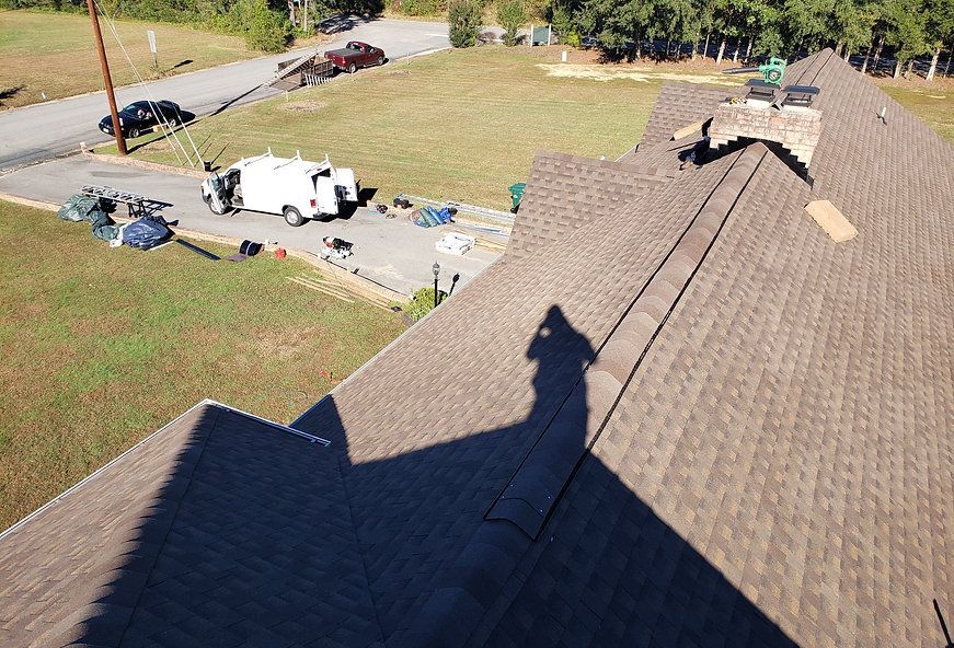 Shadow on a brown shingled roof with a chimney. A white truck and equipment are on the ground below.