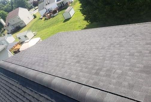 Overhead view of a gray shingled roof with a green lawn and houses in the background.