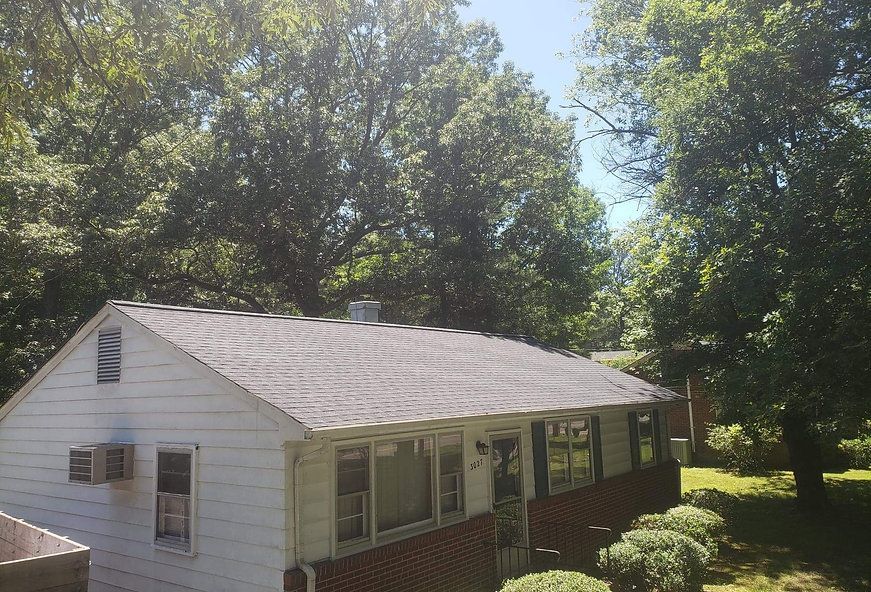 White house with a gray roof, surrounded by green trees on a sunny day.