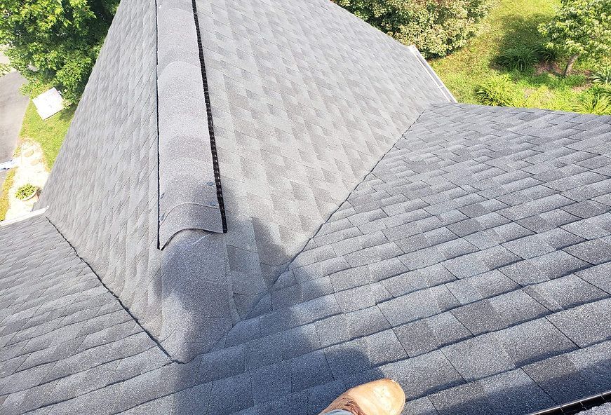Gray asphalt shingle roof with a ridge, viewed from above, sunlight.