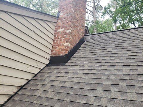 Brick chimney rising from a shingled roof with flashing where the chimney meets the roof.