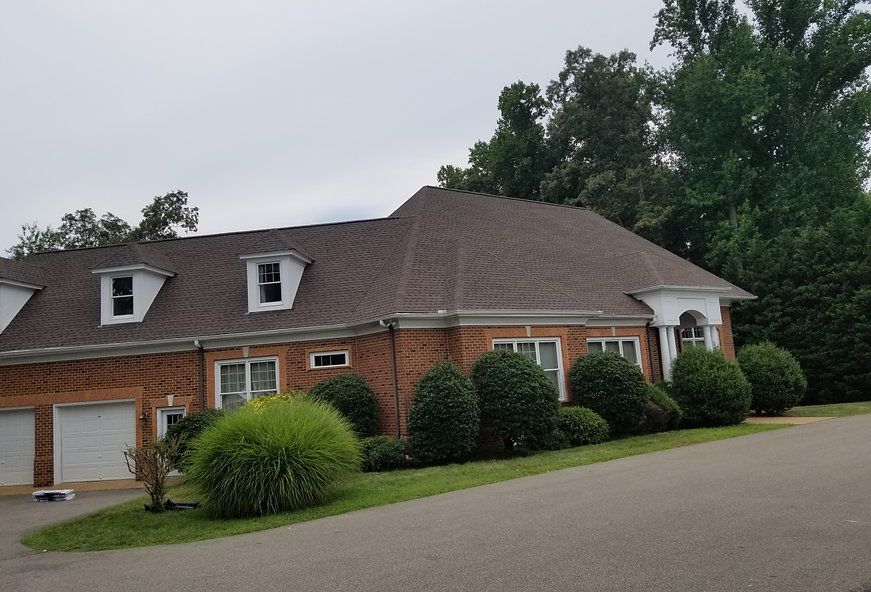 Brick house with brown roof, dormers, and white trim; green bushes line the front.